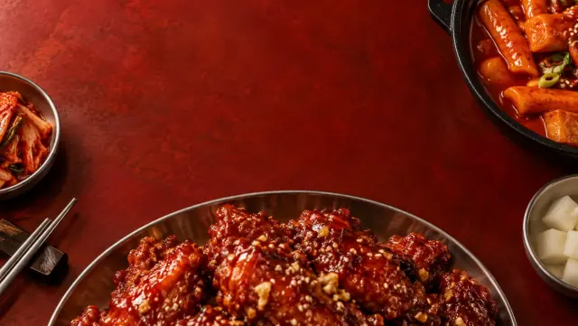 Glazed Korean fried chicken, tteokbokki and side dishes on a deep red table